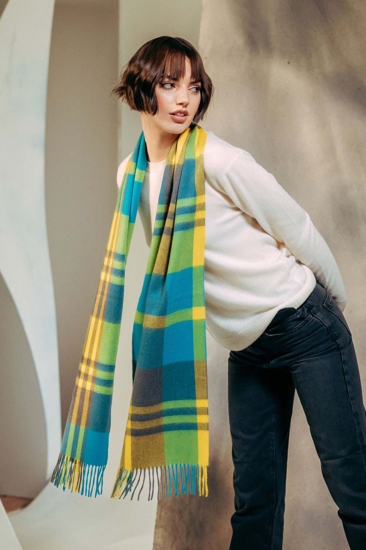 Woman wearing a colorful plaid scarf against a neutral background
