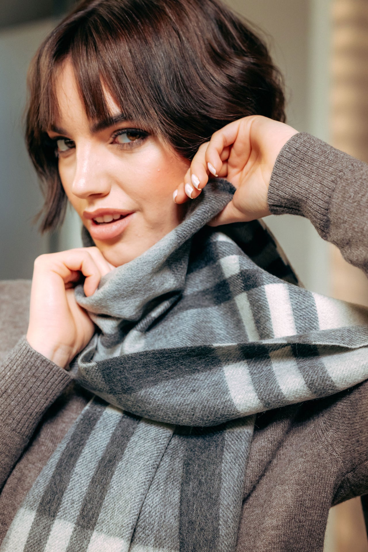 Woman wearing a gray and black checkered cashmere scarf with a blurred background
