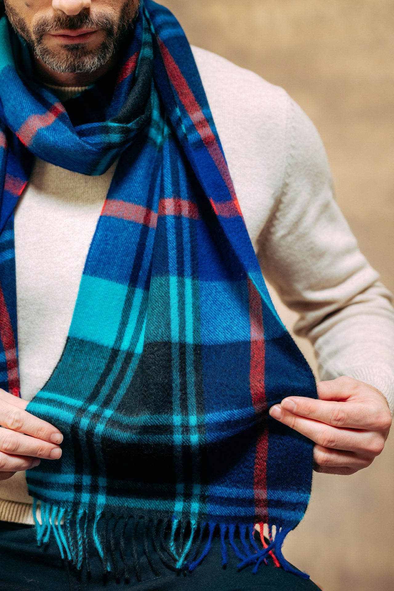 Man wearing a blue plaid cashmere scarf with a neutral background