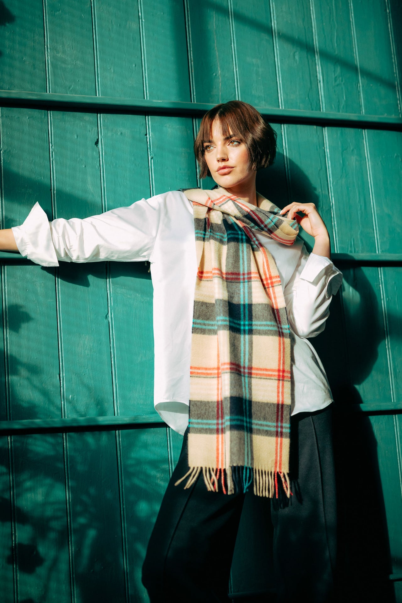 Woman wearing a plaid cashmere scarf against a teal wall