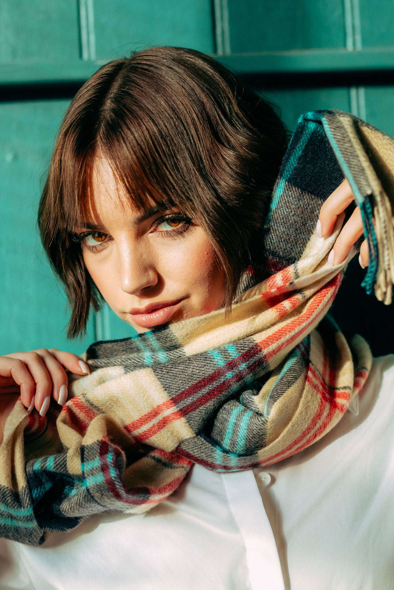 Woman holding a plaid cashmere  scarf in front of a teal door