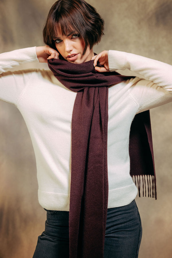 Woman wearing a white sweater and brown cashmere scarf against a neutral background