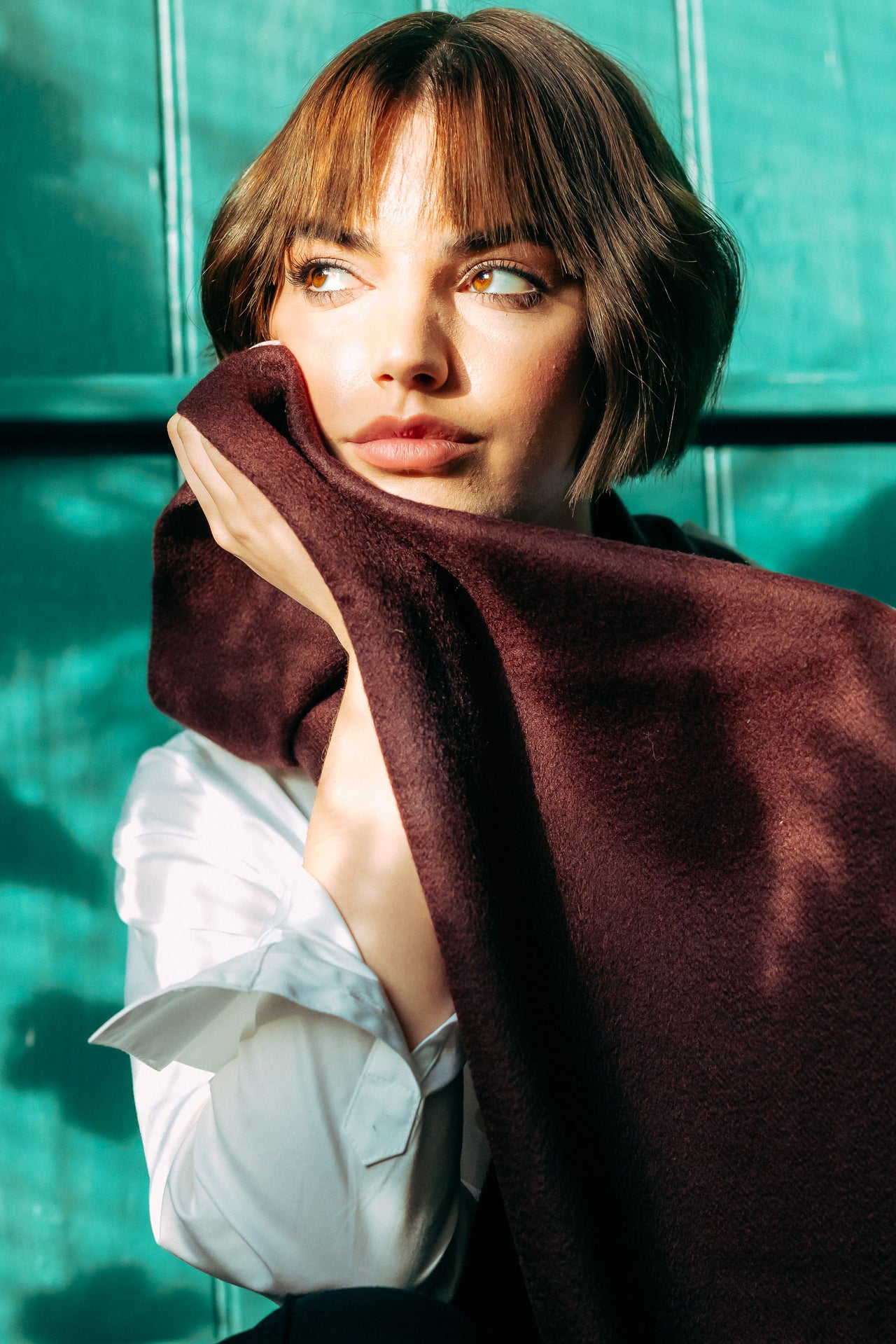 Woman holding a brown cashmere scarf in front of a green wall