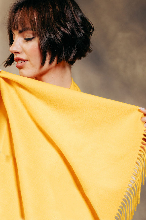 Woman holding a yellow cashmere scarf with fringe against a blurred background