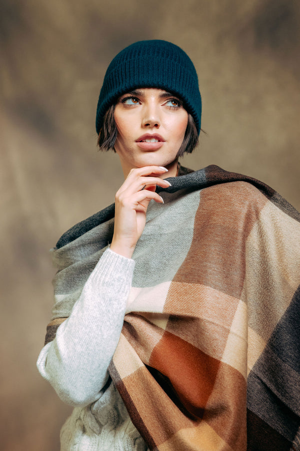 Woman wearing a blue knit hat and plaid cashmere scarf against a neutral background