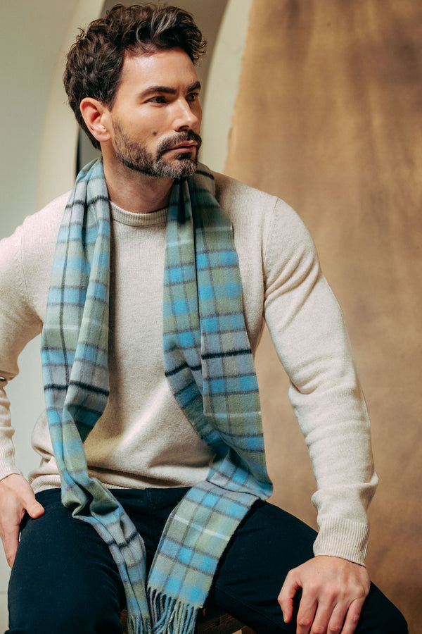 Man wearing a plaid scarf and beige sweater against a neutral background