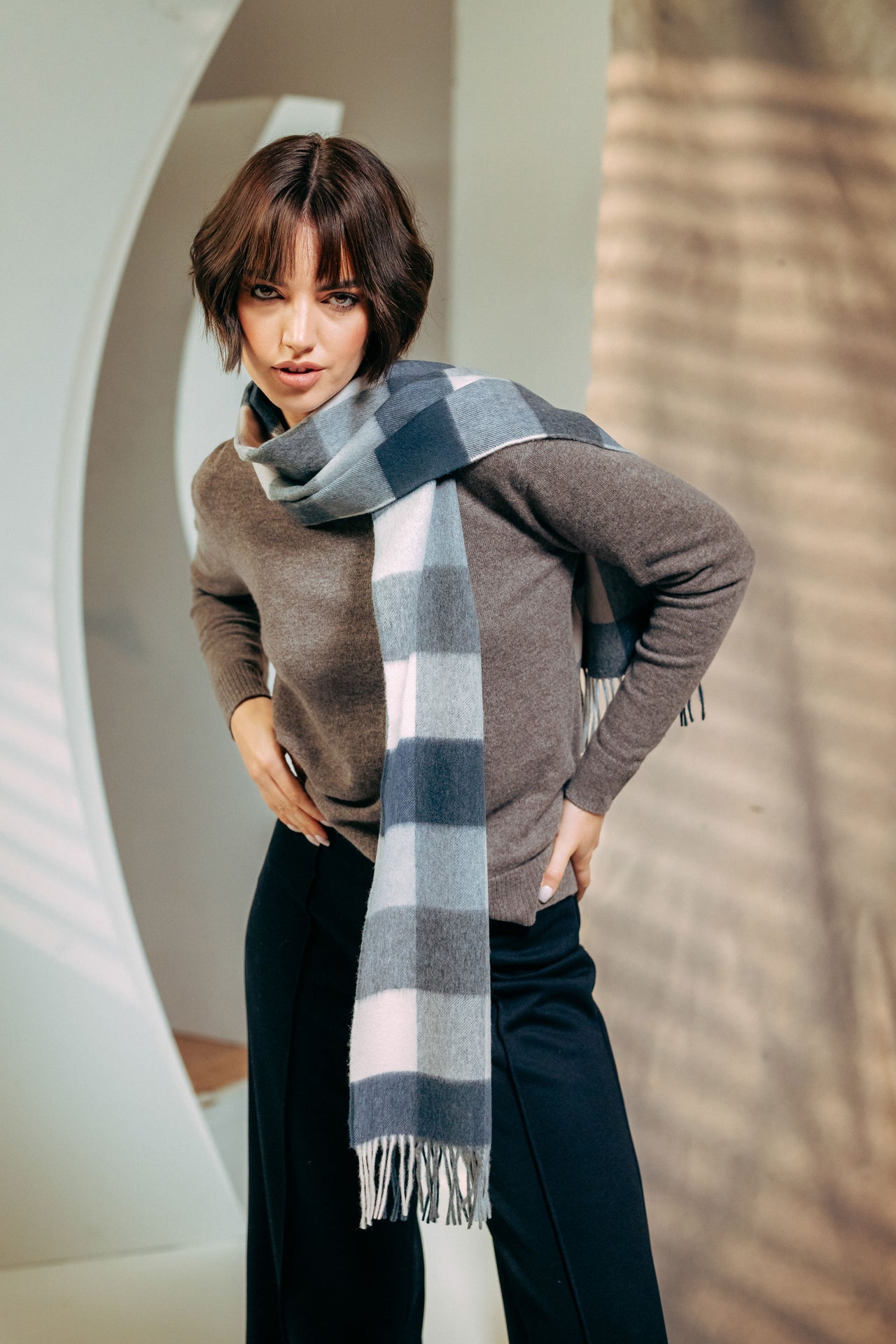 Woman wearing a gray sweater and plaid scarf in an indoor setting