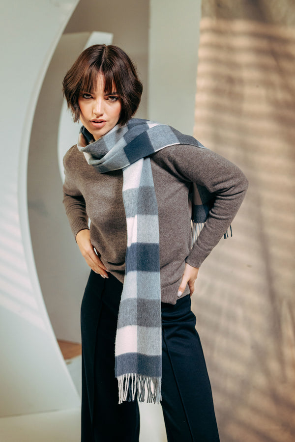 Woman wearing a gray sweater and plaid scarf in an indoor setting