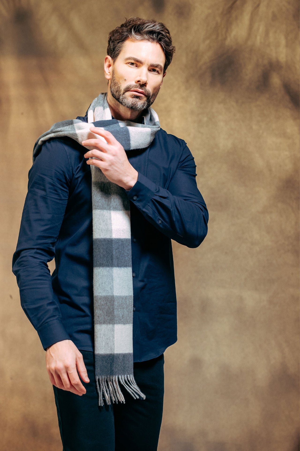 Man wearing a dark blue jacket and plaid scarf against a brown background
