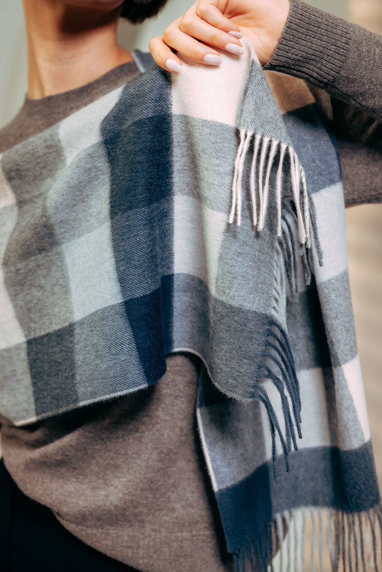 Person wearing a gray and blue plaid scarf with fringe details