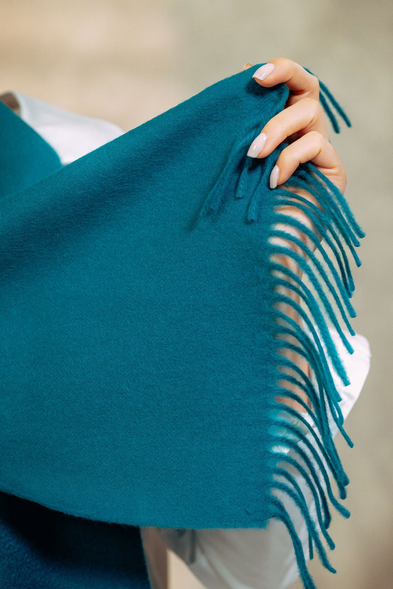 Teal shawl with fringe held by a hand against a neutral background