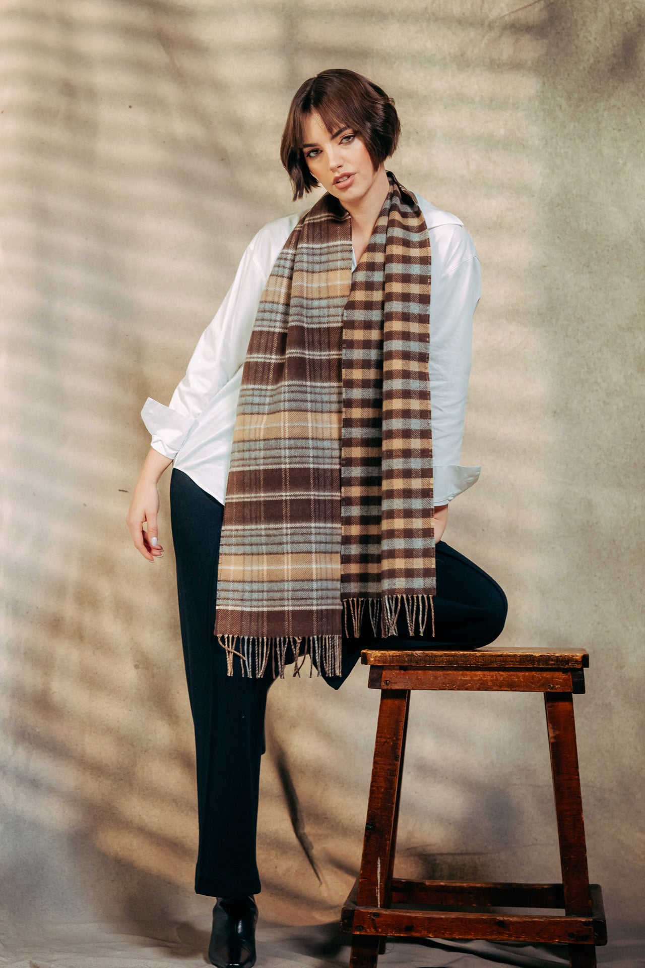 Woman wearing a plaid scarf in front of a textured wall