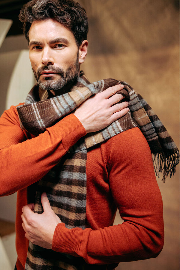 Man wearing an orange sweater and plaid cashmere scarf against a neutral background