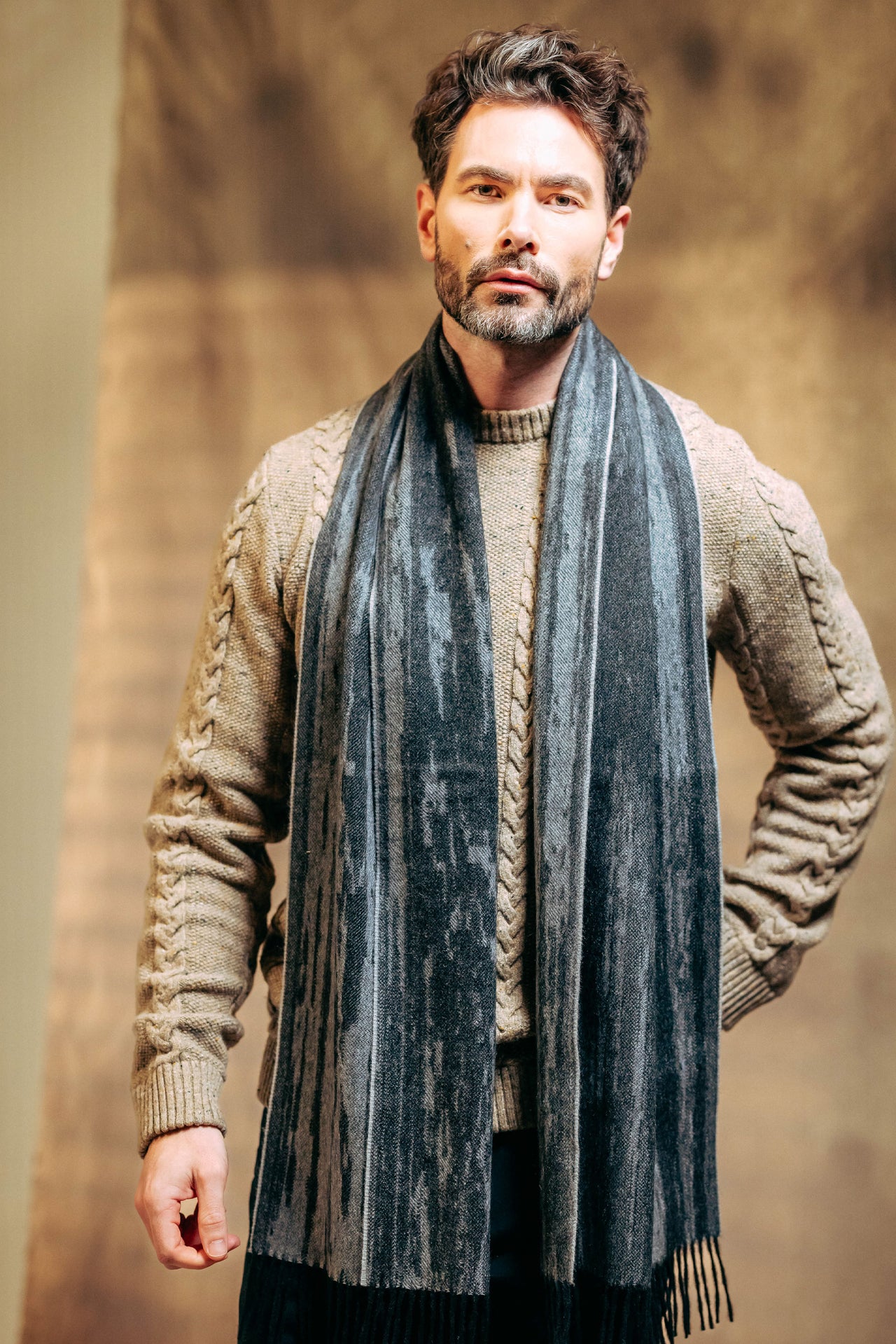 Man wearing a beige sweater and gray cashmere scarf against a brown background