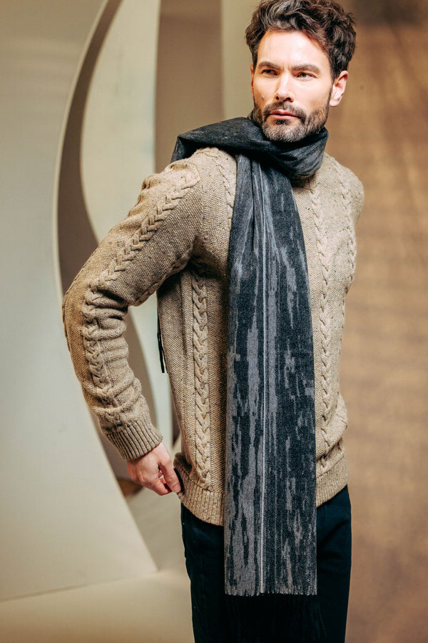 Man wearing a beige cable knit sweater and gray cashmere scarf against a neutral background