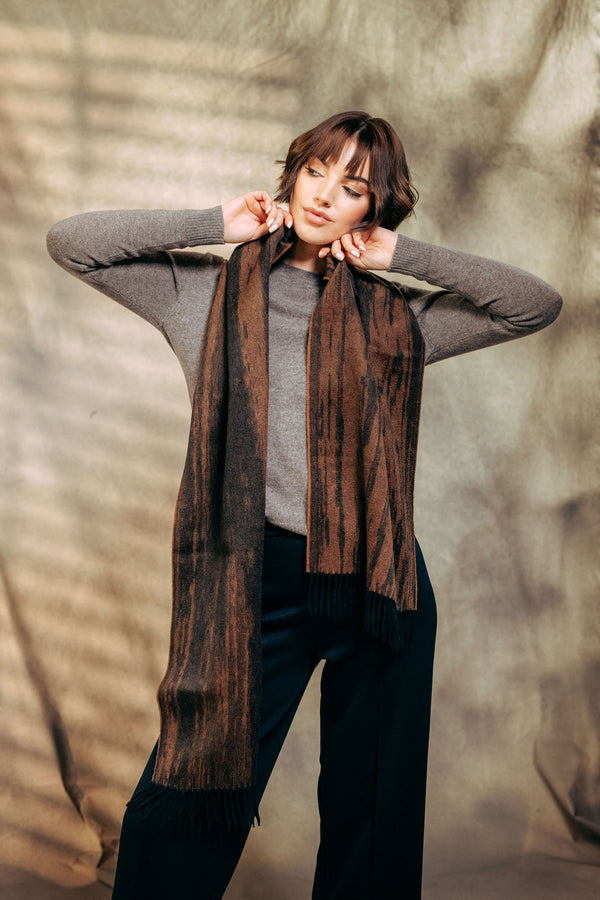 Person wearing a long brown cashmere scarf with a textured background
