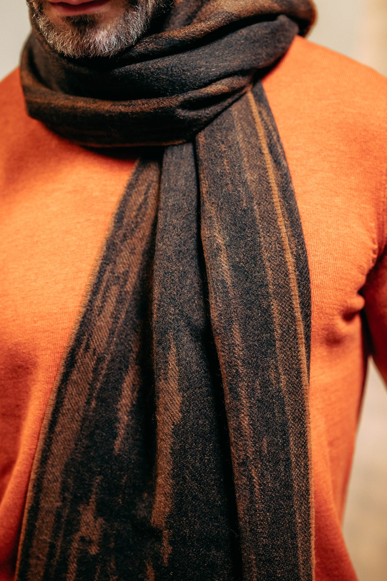 Person wearing an orange sweater and a dark brown cashmere scarf with subtle patterns.